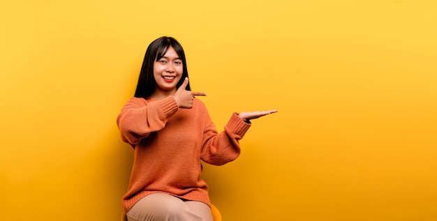 Asian girl Pretty wearing an orange casual dress. yellow background Celebrate the victory with a happy smile and the winner's expression with a raised hand. happy expression