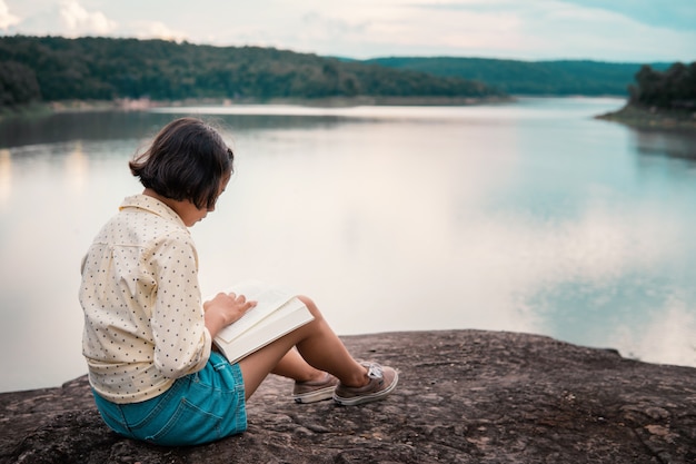 Asian girl reading a book by the lake