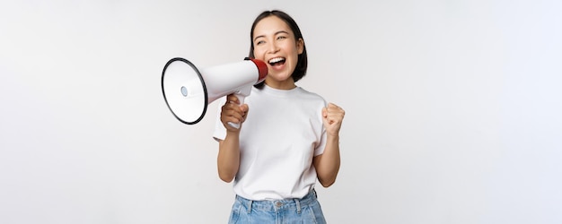 Asian girl shouting at megaphone young activist protesting using loud speakerphone making announcement white background Copy space