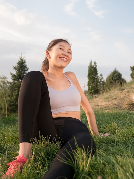 Asian girl in sportswear sits with a smile on the grass.