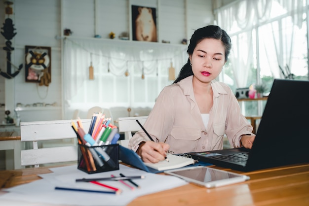 Asian girl student works using a laptop sitting at a wooden table in her own home