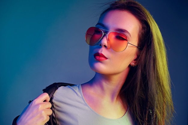 Asian girl in sunglasses and black leather jacket posing against dark blue background