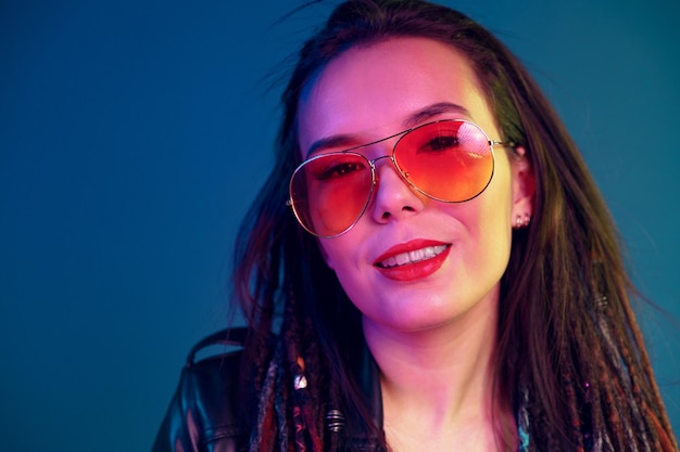 Asian girl in sunglasses and black leather jacket posing against dark blue background