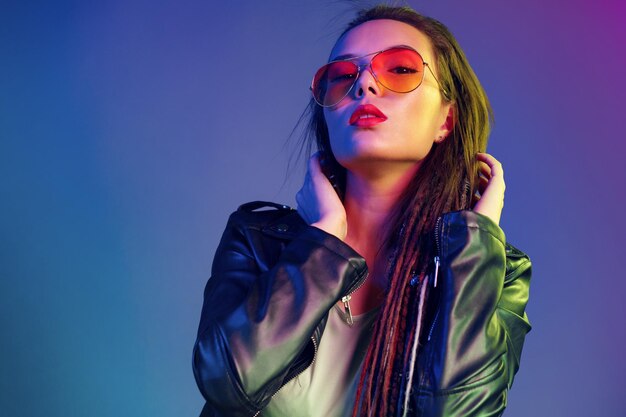 Asian girl in sunglasses and black leather jacket posing against dark blue background