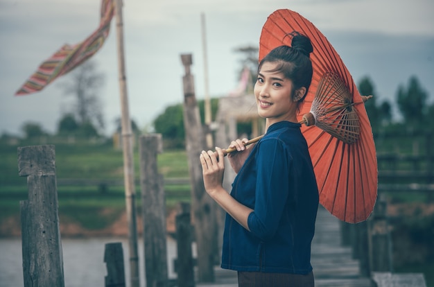 Asian girl on traditional clothes with a red umbrella crossing wooden bridge