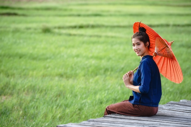 Asian girl on traditional clothes with a red umbrella sitting on a wooden bridge