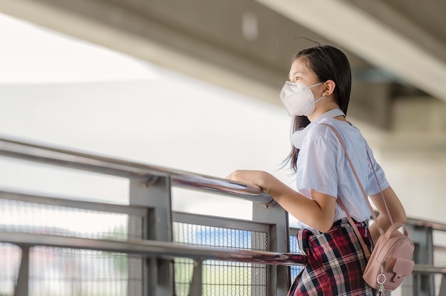 An Asian girl wearing a mask walks dejectedly on a footbridge.