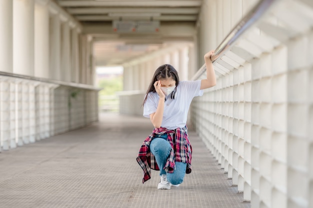 An Asian girl wearing a mask walks on an overpass with headaches, sudden fainting from debilitating conditions, and fever from coronavirus.