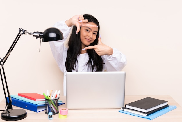 Asian girl in a workplace with a laptop on beige wall