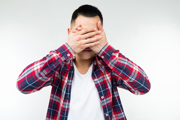 Asian guy in a checkered shirt wide open closes his eyes on an isolated white studio background.