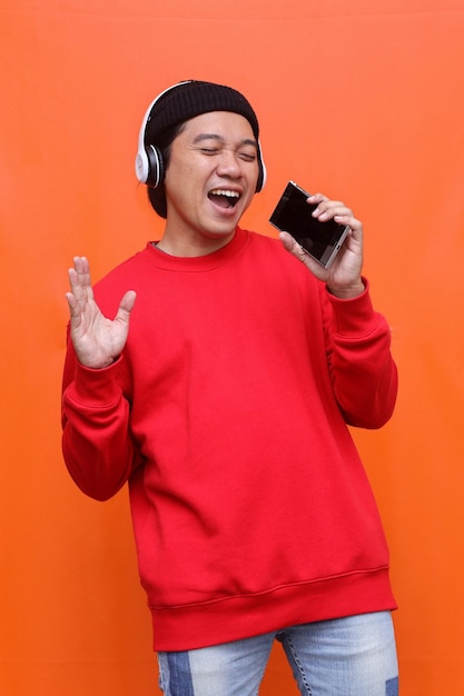 Asian guy listening music in wireless headphones and singing and using smartphone as microphone, hav