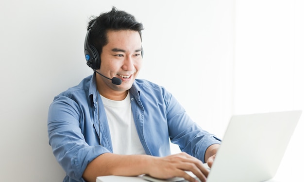 Asian handsome man in blue shirt using laptop with headphone talking smile and happy face