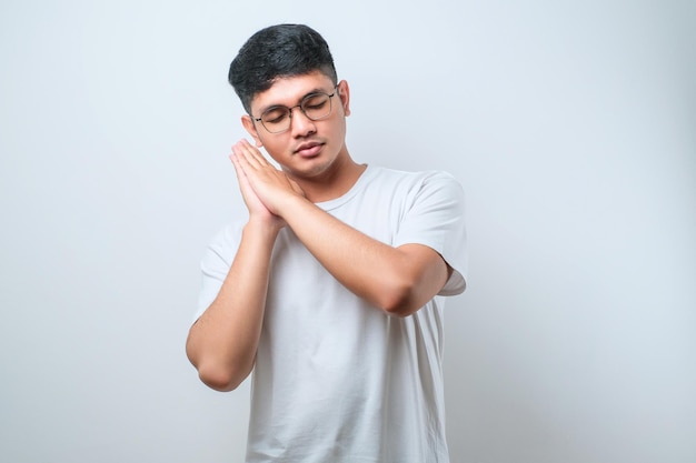 Asian handsome man wearing shirt sleeping tired dreaming and posing with hands together while smiling with closed eyes