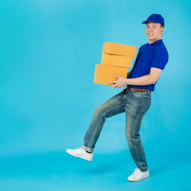 Asian happy delivery man carrying paper parcel boxes isolated on blue color wall