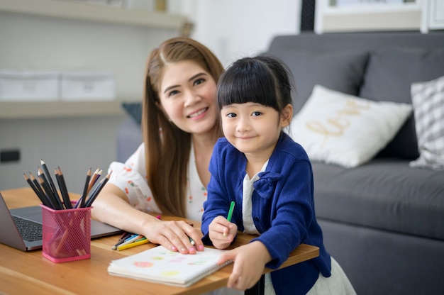 Asian Happy mom and daughter are using laptop for studying online via internet at home. E-learning Concept during quarantine time.