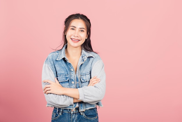 Asian happy portrait beautiful cute young woman wear denim standing her smile confidence with crossed arms isolated, studio shot on pink background and copy space, Thai female looking to camera