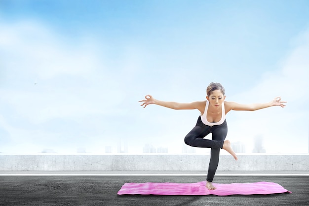 Asian healthy woman practicing yoga on the carpet at rooftop background