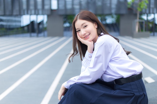 Asian high school student girl in school uniform with braces on her teeth sits and confidently.