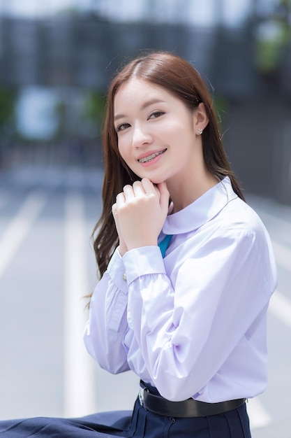 Asian high school student girl in the school uniform with braces on her teeth sits with the building