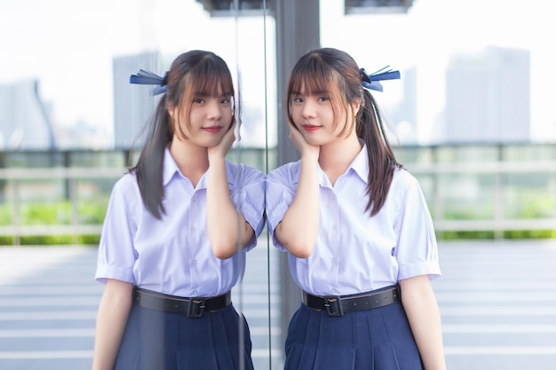 Asian high school student girl in school uniform with stands smiles confidently beside the mirror