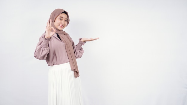 Asian hijab woman pointing blank on left side and okay isolated on white background