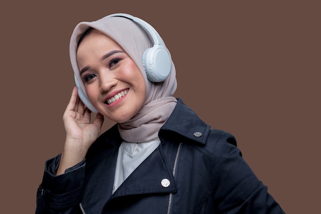 Asian hijab woman wearing wireless headphones with a smile looking at the camera