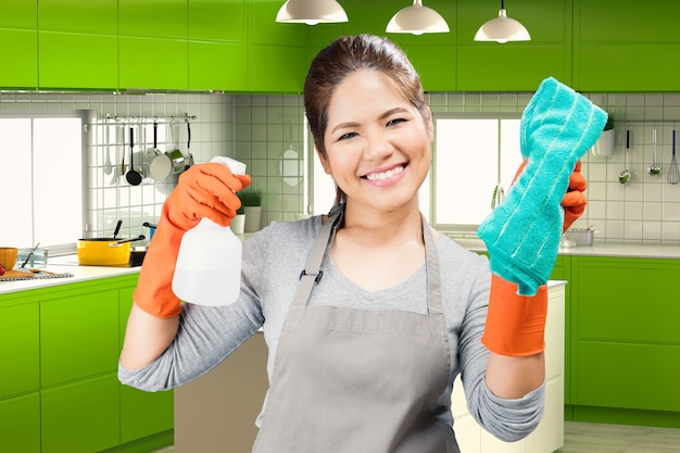 Asian housekeeper holding spray bottle and rag with kitchen background