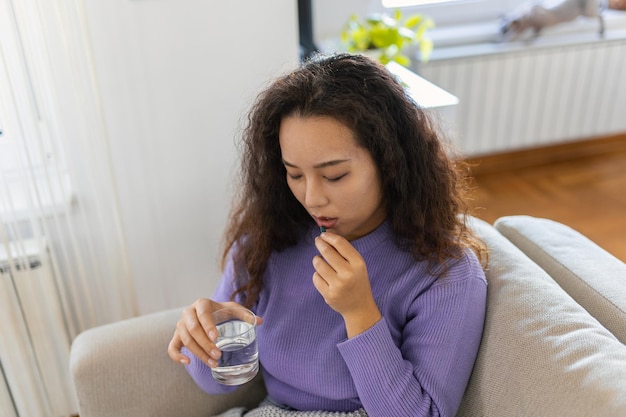 Asian ill sick woman taking painkiller medicine to relieve stomachache pain sit on bed in the morning Sick woman lying in bed with high fever Cold flu and migraine