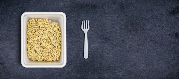 Asian instant noodles in plastic bowl with plastic disposable fork on concrete background