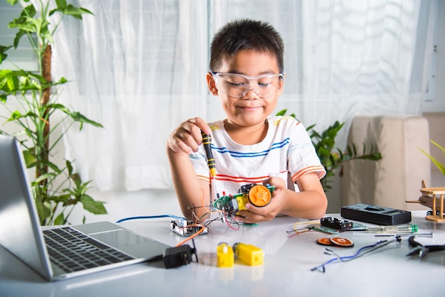 Asian kid boy assembling the Arduino robot car homework project at home