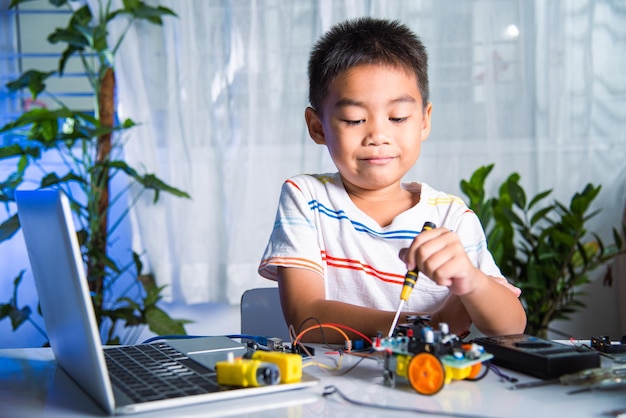 Asian kid boy assembling the Arduino robot car homework project at home