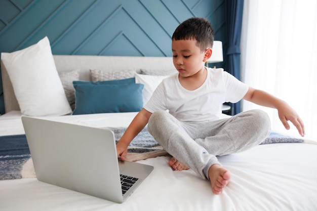 Asian kid boy using laptop study online with video call teacher at bedroom for distant learning