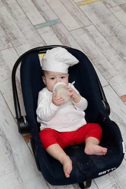 An Asian kid in a chef's hat and apron cooked Christmas ginger cookies with his mom and is now resting in his stroller and eating from a bottle