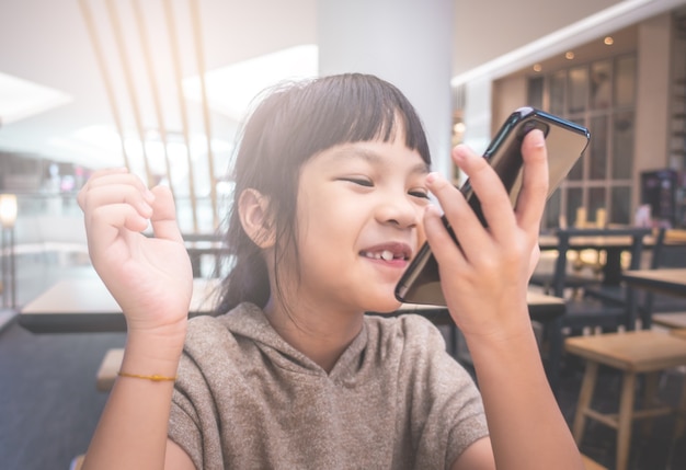 Asian kid is talking on speaker phone in cafe