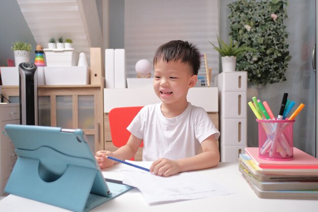 Asian kid is using tablet a tablet to study his online lesson at home