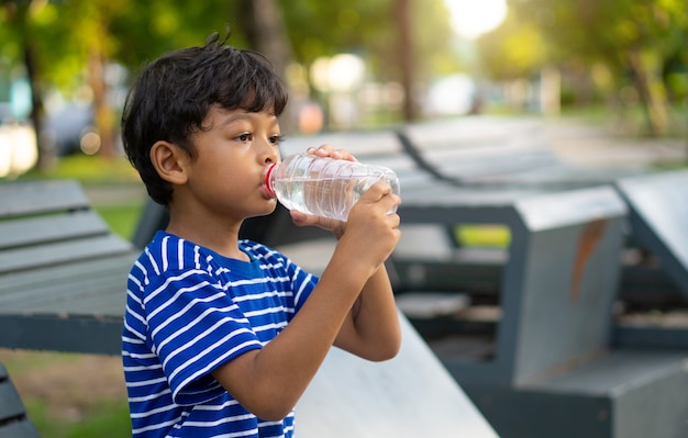 Asian kid thirsty water and drinking water from a transparent plastic bottle in the park.