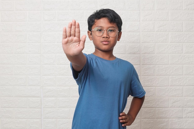 Asian kid wearing eyeglasses with open hand doing stop sign and serious expression