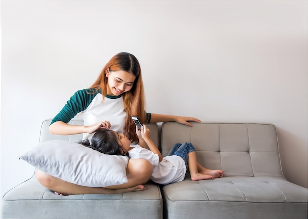 Asian kids using smartphone sitting together on sofa