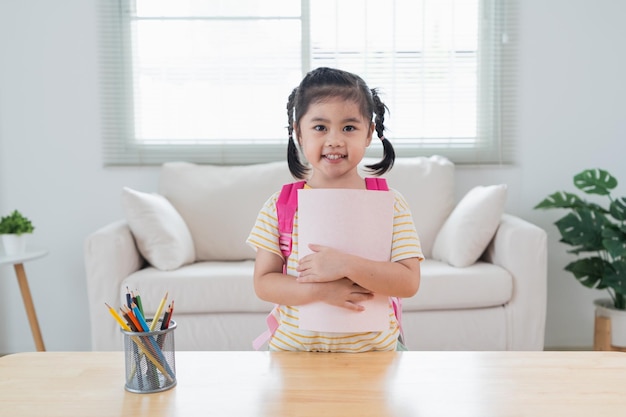 Asian kindergarten students smile backpack behind back a pink school bag and holding note book going to school for beginning of lessons excited daughter are happy go school Back to school concept