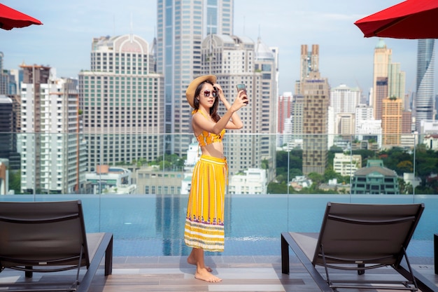 Asian lady enjoy selfie in swimming pool in rooftop of hotel in Bangkok city, Thailand