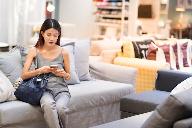 Asian lady sit on sofa and use smart mobile phone to communicate social media.