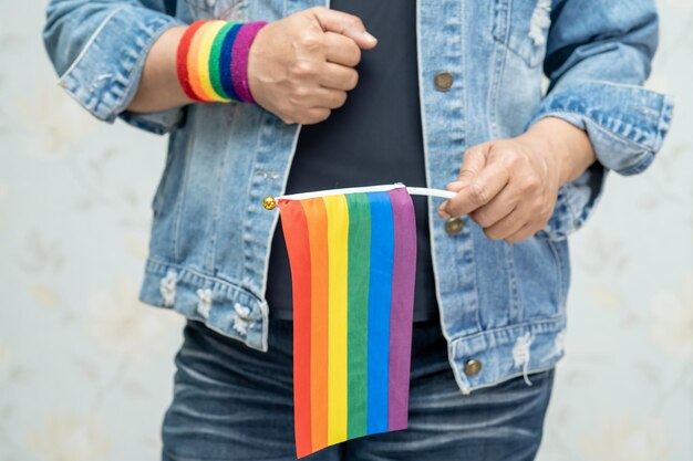 Asian lady wearing blue jean jacket or denim shirt and holding rainbow color flag, symbol of LGBT pride month celebrate annual in June social of gay, lesbian, bisexual, transgender, human rights.