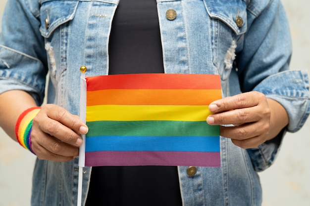 Asian lady wearing blue jean jacket or denim shirt and holding rainbow color flag, symbol of LGBT pride month.