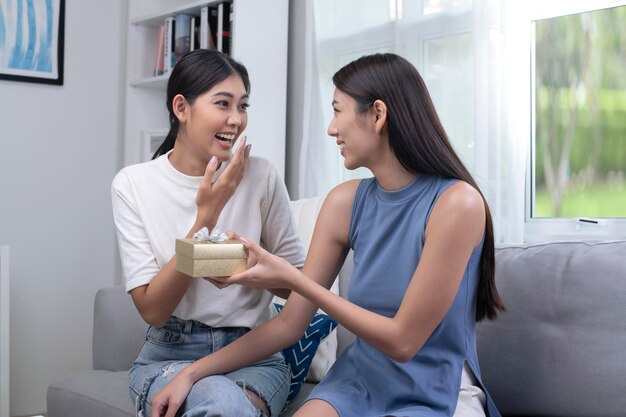 Asian lesbian woman congratulates her girlfriend on birthday LGBT woman makes surprise gives to beloved woman gift box with present family celebrating life events LGBT couple lifestyle concept