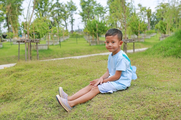 Asian little boy child looking camera and sitting on green grass in the garden