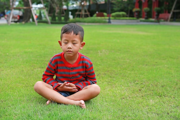 Asian little boy child practicing mindfulness meditation sitting on lawn in the garden