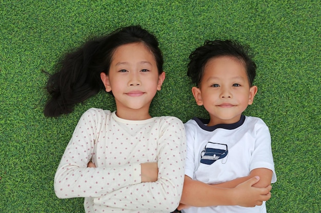 Asian little boy and girl child lying on green grass background together with looking camera Above view