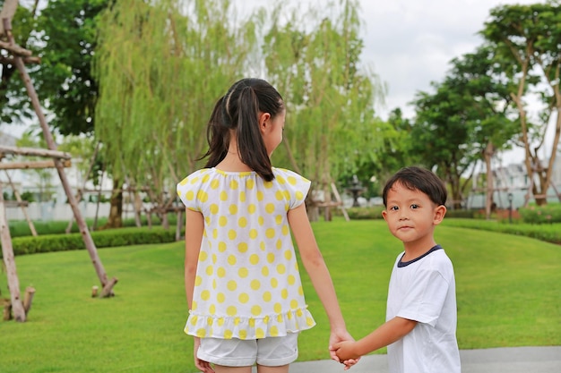 Asian little boy and girl child with hand in hand while play together in the garden Asian Children in green park