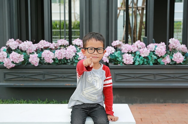 Asian little boy pointing at camera while sitting in the garden