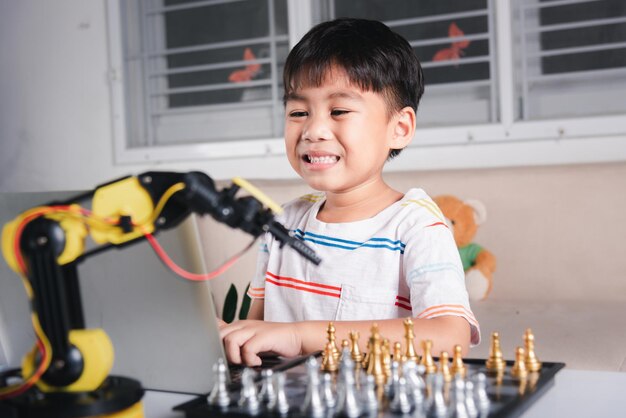 Asian little boy programming code to robot machine arm on laptop for play chess